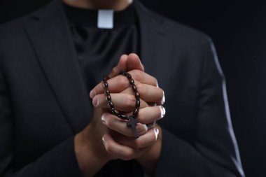 Siyah arka planda tespih çeken rahip, yakın plan.