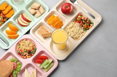 Okul yemeği. Lezzetli yiyecekli plastik tepsiler ve gri masada portakal suyu, üst manzara. Metin için boşluk