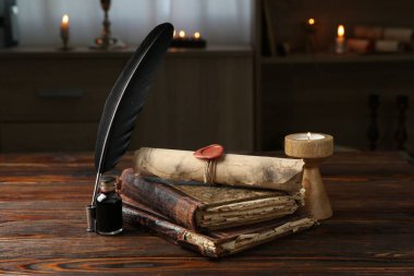Yuvarlanmış parşömen, yanan mum, tüy, mürekkep hokkası ve ahşap masadaki kitaplar.