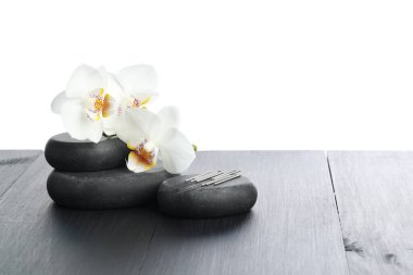 Akupunktur iğneleri, orkide çiçekleri ve beyaz arka plana karşı gri ahşap masa üzerindeki spa taşları