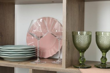 Beyaz duvarın yakınındaki raflarda farklı tabaklar ve bardaklar var.