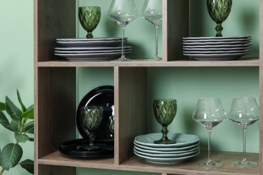 Kapalı alandaki yeşil duvarın yanında farklı plaka ve gözlüklerle raf ünitesi.