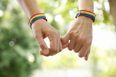 LGBT konsepti. Gökkuşağı bileklikli kadınlar dışarıda el ele tutuşuyorlar, yakın plan.