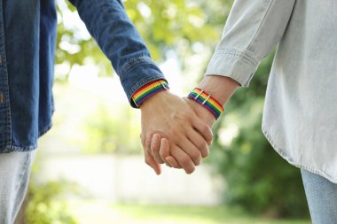 LGBT konsepti. Gökkuşağı bileklikli kadınlar dışarıda el ele tutuşuyorlar, yakın plan.