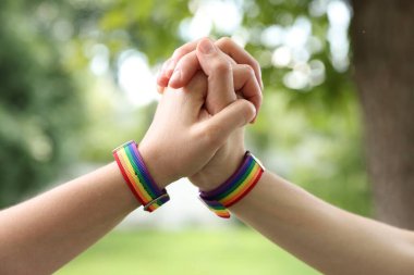 LGBT konsepti. Gökkuşağı bileklikli kadınlar dışarıda el ele tutuşuyorlar, yakın plan.