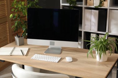 Modern bilgisayarı, kırtasiyesi ve çiçek dekoru olan şık bir iş yeri. Biyofilik iç tasarım