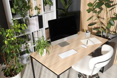 Modern bilgisayarı, kırtasiyesi ve çiçek dekoru olan şık bir iş yeri. Biyofilik iç tasarım