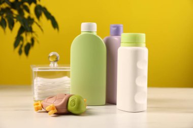 Bebek aksesuarları ve banyo ürünleri beyaz mermer masada, sarı arka planda.