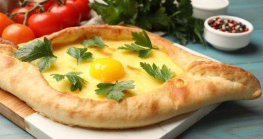 Peynirli, yumurtalı, maydanozlu, domatesli ve baharatlı leziz khachapuri. Açık mavi ahşap masa, yakın plan.