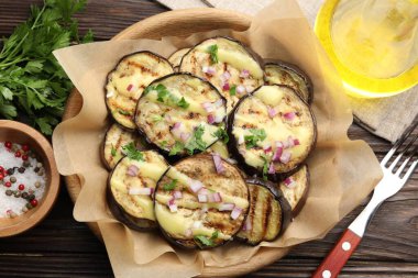 Ahşap masada servis edilen soslu, maydanozlu ve soğanlı ızgara patlıcan dilimleri.