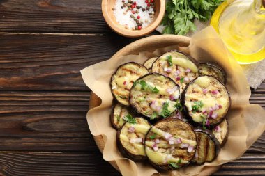 Ahşap masada servis edilen soslu, maydanozlu ve soğanlı ızgara patlıcan dilimleri. Metin için boşluk