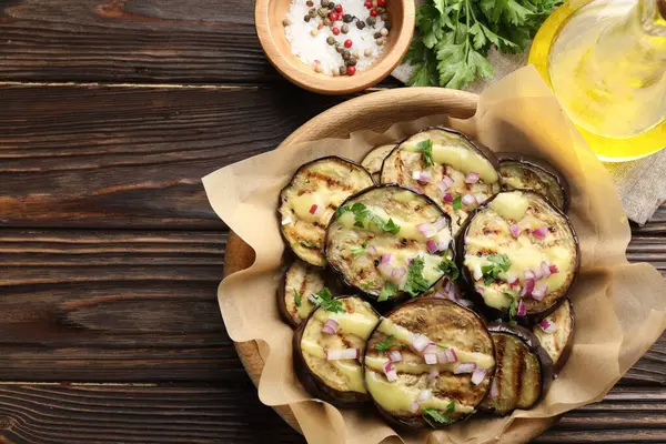 Ahşap masada servis edilen soslu, maydanozlu ve soğanlı ızgara patlıcan dilimleri. Metin için boşluk
