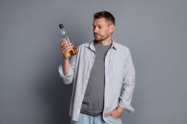 Gri arka planda akşamdan kalma viski şişesi olan bir adam.