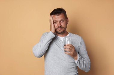 Bir bardak suyu olan bir adam bej arka planda akşamdan kalma.