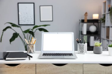 Ofisteki beyaz masada dizüstü bilgisayarı ve kırtasiyesi olan şık bir iş yeri.