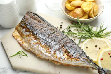 Beyaz mermer masanın üstünde baharat ve patatesle servis edilen kızarmış uskumru. Ev yapımı deniz ürünleri yemeği.