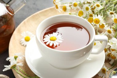 Lezzetli papatya çayı ve çiçekler siyah masada, yakın plan.