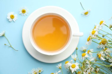 Lezzetli papatya çayı ve çiçekler açık mavi arka planda, düz yerde