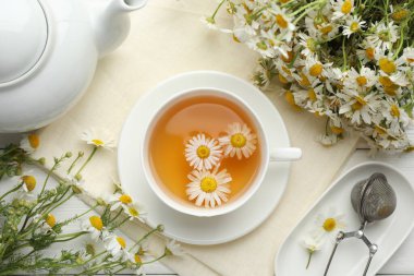 Lezzetli papatya çayı, zerk makinesi ve çiçekler beyaz ahşap masada, düz uzanmış.