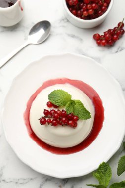 Kırmızı üzümlü lezzetli panna cotta, beyaz mermer masa üzerinde sos ve nane, düz yatıyordu.