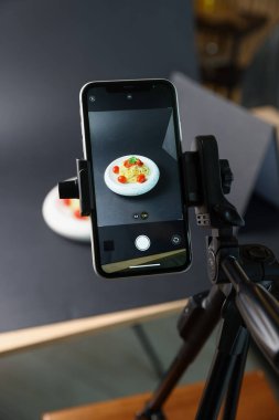 Stüdyoda akıllı telefonla lezzetli makarna çekmek, ekrana odaklanmak. Profesyonel yemek fotoğrafçılığı.