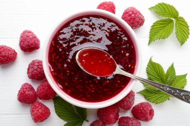 Tatlı ahududu reçeli kasede, böğürtlen ve yeşil yapraklar beyaz ahşap masada, düz yerde