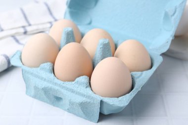 Yumurta kartonunda çiğ tavuk yumurtası, beyaz fayanslı masa, yakın plan.