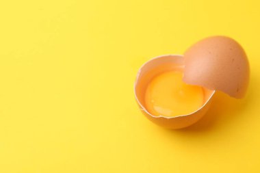 Sarı arka planda kırılmış bir tavuk yumurtası, yakın plan. Metin için boşluk