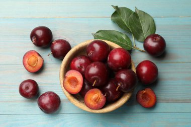 Olgun kiraz erikleri, kase ve yeşil yapraklar açık mavi ahşap masa, düz uzanmış