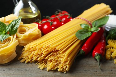 Farklı türde makarna ve malzemeler ahşap masada, yakın plan.