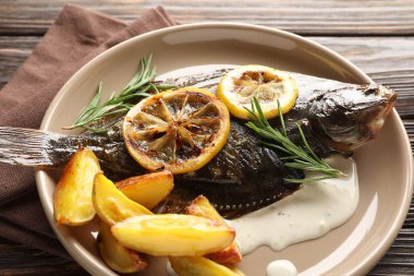 Biberiye, patates ve limon dilimleri ile ahşap masada kızarmış balık, yakın plan. Ev yapımı deniz ürünleri yemeği.