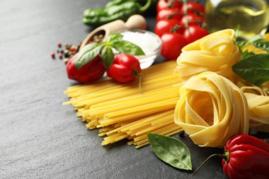 Farklı türde makarna ve malzemeler siyah masada, yakın plan. Metin için boşluk