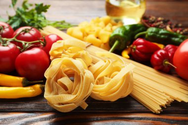 Farklı türde makarna ve malzemeler ahşap masada, yakın plan.