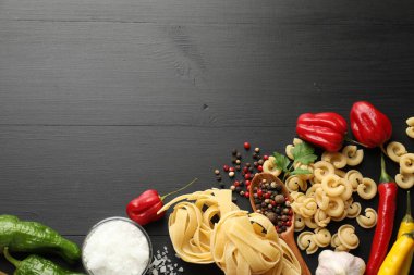Farklı türde ham makarna, ürünler ve baharatlar siyah ahşap masa üzerinde, düz yatak. Metin için boşluk