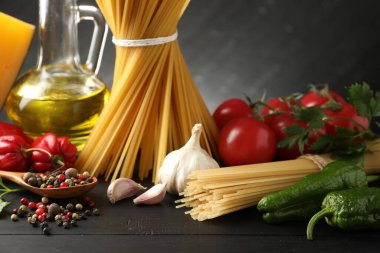 Çiğ spagetti makarna, ürünler ve baharatlar siyah ahşap masa üzerinde, yakın plan