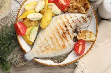 Hafif ahşap masada patates, domates ve limon dilimleriyle servis edilen kızarmış balık. Ev yapımı deniz ürünleri yemeği.