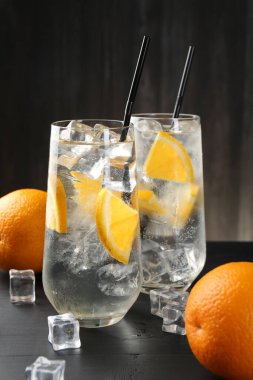 Portakal dilimleri ve siyah ahşap masa üzerindeki buz küpleriyle soda tazeleniyor.