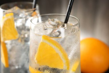 Portakal dilimli soda ve bulanık arkaplanda buz küpleri, yakın plan.