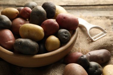 Tabaktaki farklı patatesler ve ahşap masadaki soyucular, yakın plan.