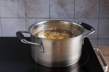 Tencerede taze makarna ve elektrikli ocakta su, yakın plan.