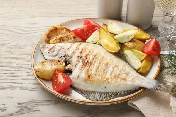 Hafif ahşap masada patates, domates ve limon dilimleriyle servis edilen kızarmış balık, yakın plan. Ev yapımı deniz ürünleri yemeği.