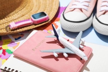 Yaz tatili zamanı. Pasaport, defter, oyuncak uçak, akıllı saat, ayakkabılar, hasır şapka ve dünya haritası masada.