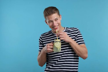 Mason kavanozundan açık mavi arka planda limonata içen gülümseyen adam. Tazeleyici içecek.