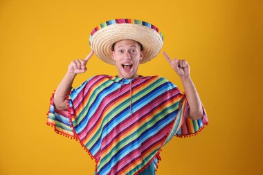 Renkli pançolu duygusal adam sarı arka plandaki şapkasını işaret ediyor.