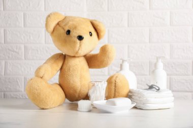 Tuğla duvarın yanında bir sürü bebek aksesuarı ve oyuncak ayı var.