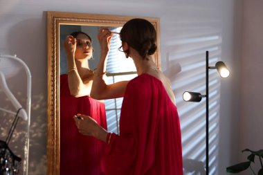 Güzel bir kadın aynanın yanında hazırlanırken makyaj yapıyor.