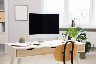 Ofisteki beyaz masa üzerinde modern bilgisayarı ve kırtasiyesi olan şık bir iş yeri.