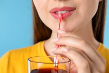 Açık mavi arka planda samandan meyve suyu içen kadın, yakın plan.