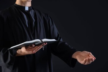 Kutsal İncil 'i olan ve siyah arka planda vaaz veren bir rahip, yakın plan.