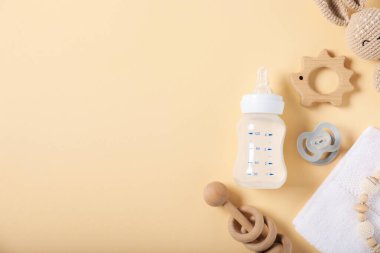 İçinde süt ve bej arka planda bebek aksesuarları olan bir şişe. Metin için boşluk